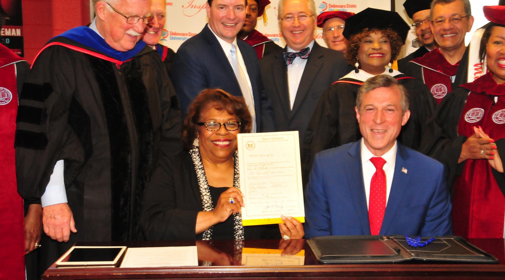<p>Interim DSU President Wilma Mishoe holds the legislation just signed May 12 by Gov. John Carney (seated next to her) that adds a fourth year of state funding to the Inspire Scholarship Program.</p>
