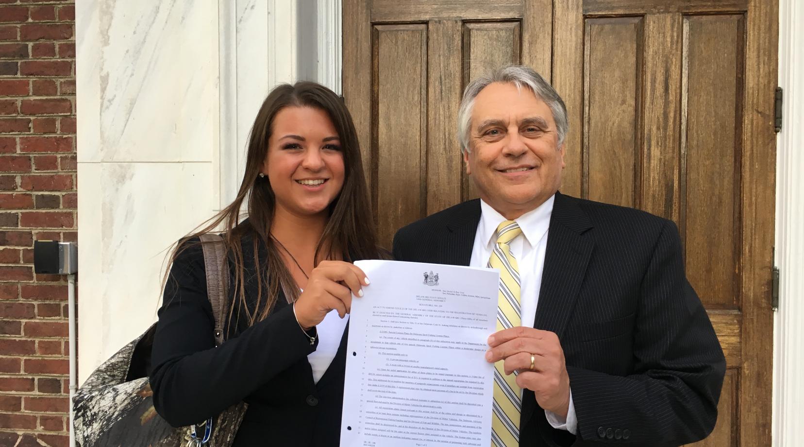 Caitlin Berchtold, a junior DSU fisheries management major, and David Saveikis, director of the state Division of Fish and Wildlife, hold Senate Bill 220 after the House unanimously passed it on June 27. Ms. Berchtold proposed the legislation, which will create license plates of which the proceeds will benefit fisheries research and recreational fisheries.
