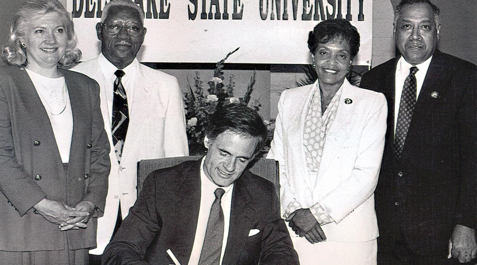 Dr. Willliam B. DeLauder (far right), the University's eighth president, stands with state Rep. Nancy Wagner, state Sen. Herman Holloway Sr., and his wife Vermell, as then-Gov Tom Carper signed legislation renaming the College to Delaware State University. Dr. DeLauder passed away on May 21.