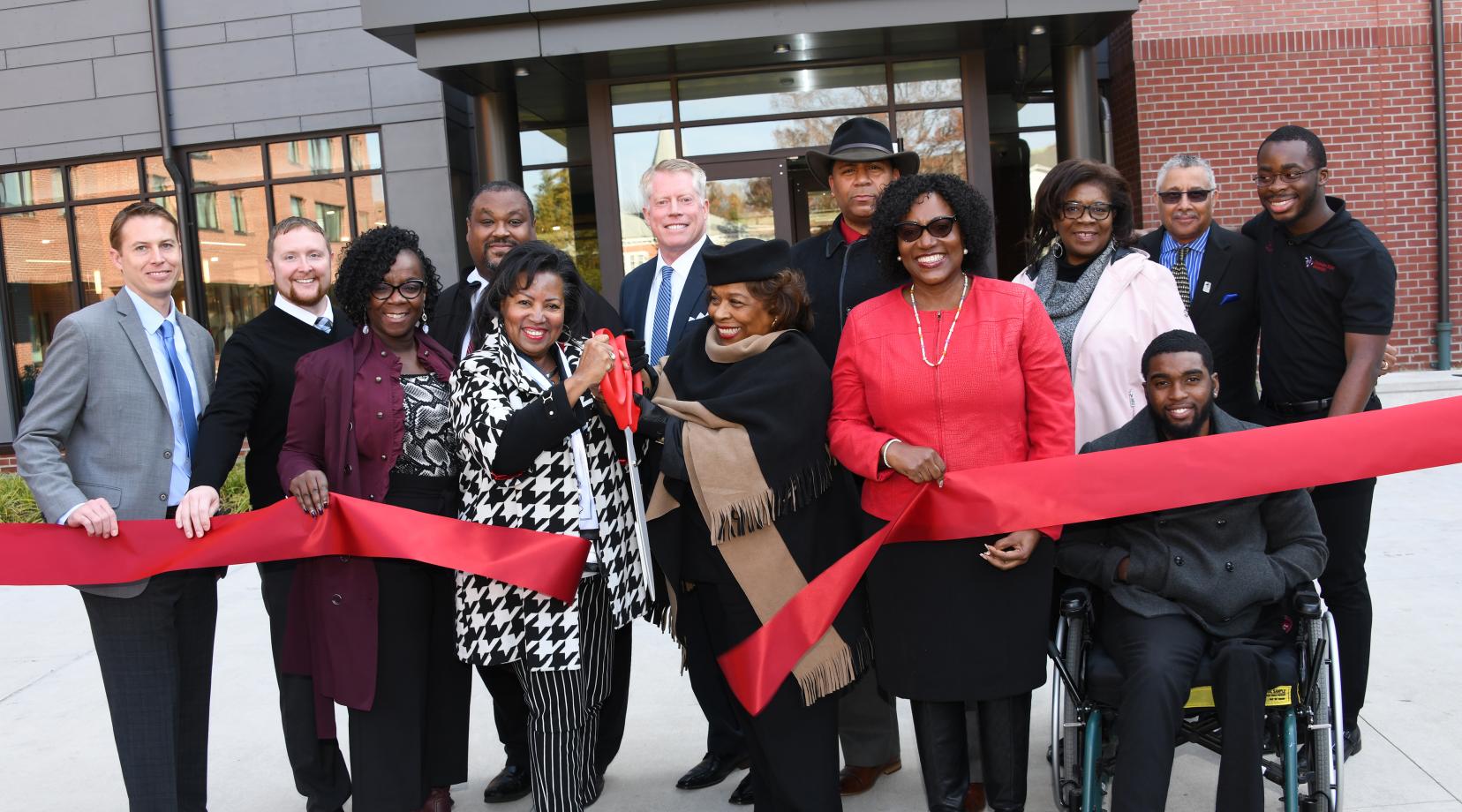 Dr. Devona Williams (with scissors) and University President Wilma Mishoe and others take part in the ribbon-cutting ceremony to formally christen the new Tubman-Laws Residential Hall.
