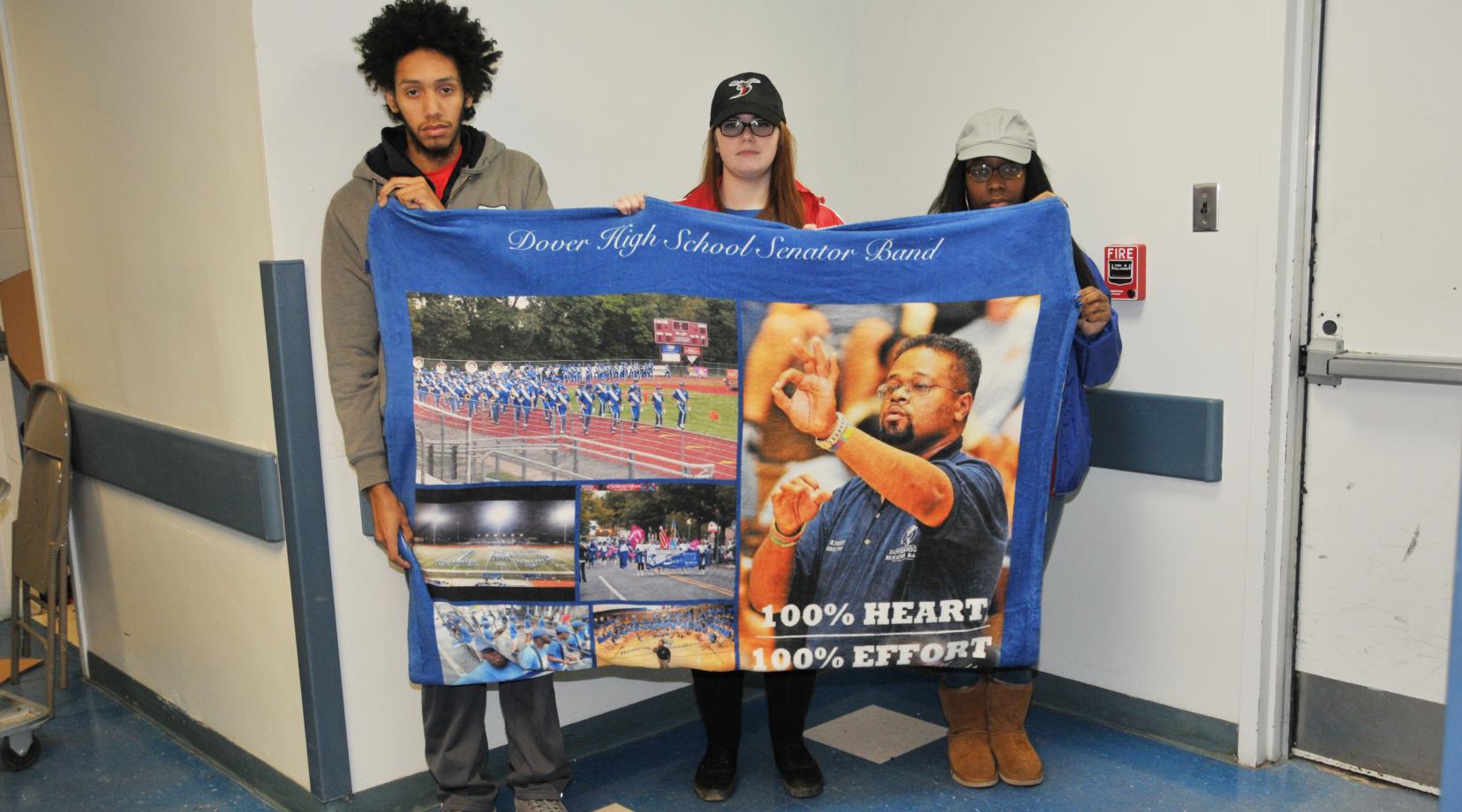 (L-r) Carlos Ortiz, Christina Trice and Akeya Rainer, former Dover HS Band members who were under Lenny Knight's director and then followed him to DSU, hold up a blanket of images that Dover HS presented to Mr. Knight at the end of his tenure there.