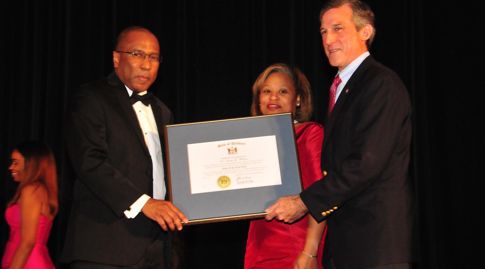 Dr. Harry L. Williams (l), joined by his wife Dr. Robin Williams, receives the Order of the First State from Delaware Gov. John Carney during the Dec. 9 President's Scholarship Ball.