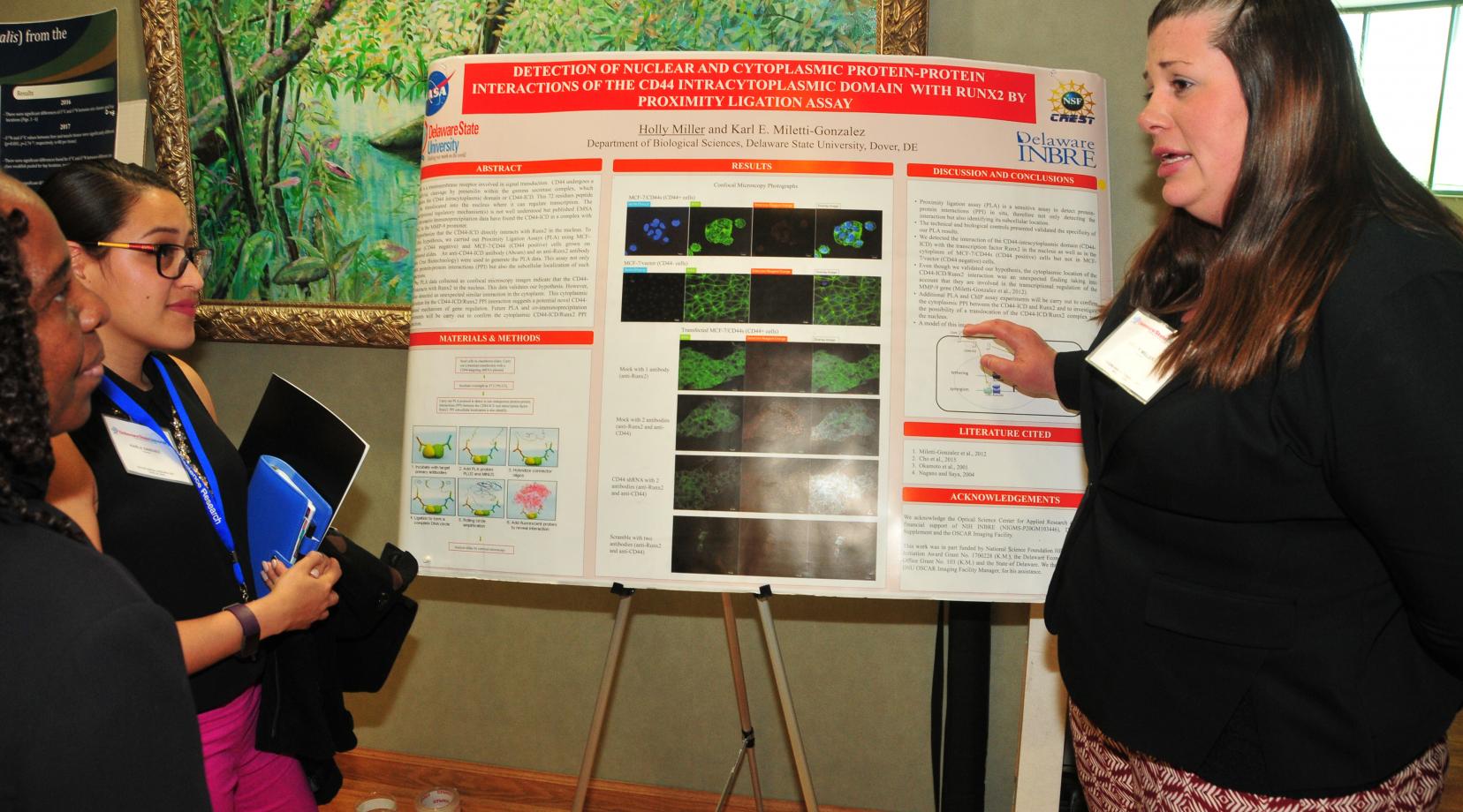 <p>Holly Miller, a biological science graduate students, explains her research poster on the detection of nuclear and cytoplasmic protein and the protein interaction of the CD44 intracytoplasmic domain with RUNX2 by proximity ligation assay.</p>