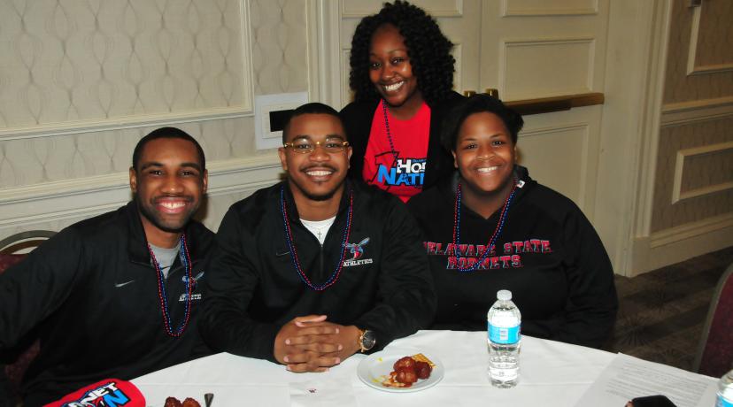 <p>Diane Kirby (standing), manager of DSU Alumni Engagement, poses with three young alums at the March 9 DSU Alumni Reception at the MEAC Tournament in Norfolk, Va.</p>