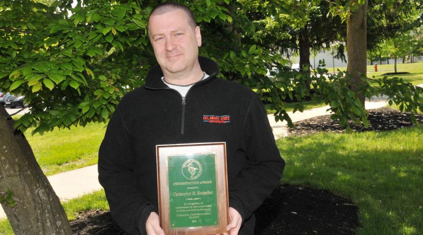 <p>Dr. Christopher Heckscher, associate professor of environmental sciences, holds the Conservation Award he recently receives from the Delmarva Ornithological Society.</p>